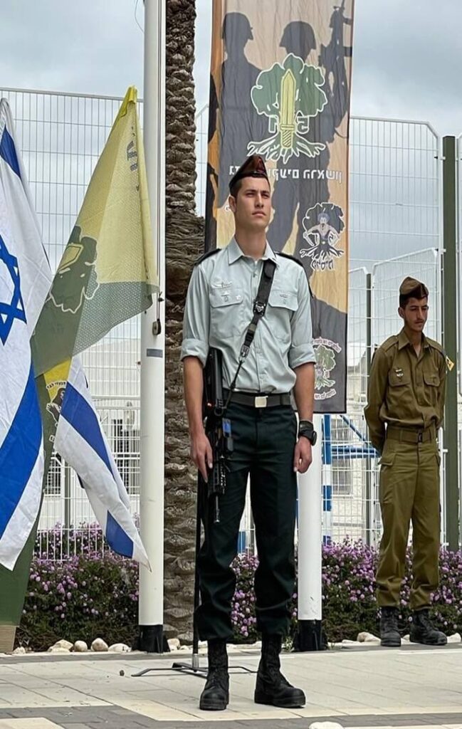 בן עומד בטקס לצד דגלי ישראל